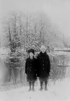 2 flickor stående vid vattendrag.
Nyckelord: Vinter