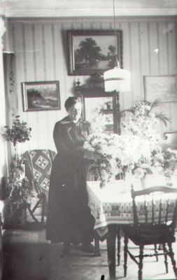 Kvinna stående vid bord i rum.
Nyckelord: Tavla Lampa Blommor