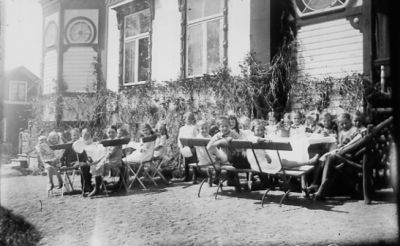 Ett antal barn sittande runt trädgårdsbord.
Nyckelord: Skolklass Trädgårdsmöbel