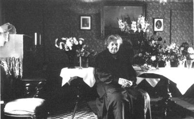 Kvinna sittande i rum bland blommor.
Nyckelord: Blommor Tapet Tavla