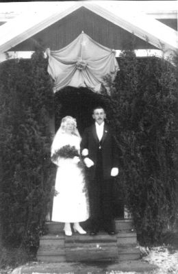 Brudpar stående framför byggnad.
