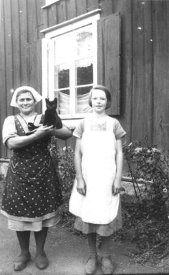 Kvinna stående med katt på armen och flicka stående framför byggnad.
Nyckelord: Katt Fönster Bostad