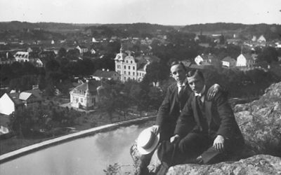 2 män sittande på berg med vattendrag och stadsvy i bakgrunden.
Nyckelord: Utsikt