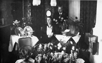 Man stående och kvinna sittande i rum med blommor och presenter.
Nyckelord: Födelsedag Blommor Presenter