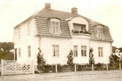 Man och kvinna på balkong till putsad villa utmed gata
Nyckelord: Grind