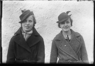 2 kvinnor stående framför vägg.
Nyckelord: Hatt