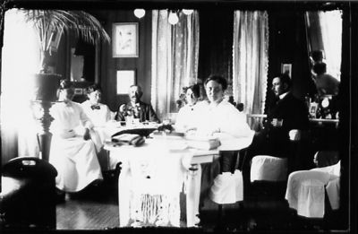 2 män och 4 kvinnor sittande vid bord i rum.
