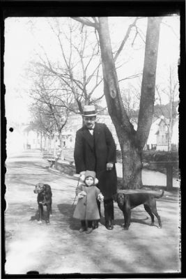 Man, flicka och 2 hundar stående på gång intill vattendrag och med byggnader i bakgrunden.
Keywords: Hund
