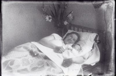 Kvinna och spädbarn liggande i säng.
Nyckelord: Säng Blommor