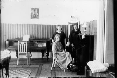 2 kvinnor stående och 1 kvinna sittande vid piano i lokal.
Nyckelord: Piano Flygel