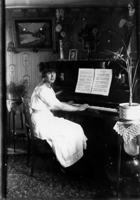 Kvinna sittande vid piano.
Nyckelord: Piano Pedistal Tapet