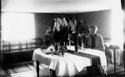 Kvinna sittande vid bord med blommor på.
Nyckelord: Interiör Blommor