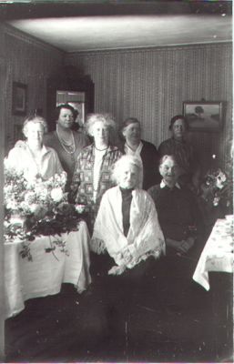 5 kvinnor stående och 2 sittande i rum.
Nyckelord: Blommor Spegel