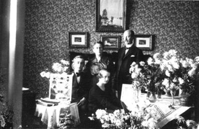 Man och kvinna stående, pojke och flicka sittande i rum.
Nyckelord: Högtid Blommor Tavla