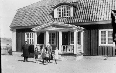 Man, kvinna, 2 pojkar och 2 flickor stående framför byggnad.
Nyckelord: Grusplan Veranda