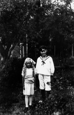Pojke och flicka stående i trädgård.
Nyckelord: Skogsbacke Skog Dräkt
