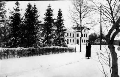 Kvinna stående i snön på väg med byggnad i bakgrunden.
Nyckelord: Vinter