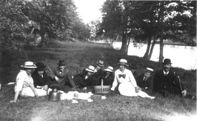 7 män och 2 kvinnor sittande i gräset intiill vattendrag.
Nyckelord: Picnic