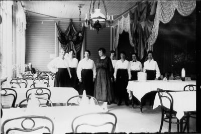 8 kvinnor stående bland serveringsmöbler.
Nyckelord: Matsal
