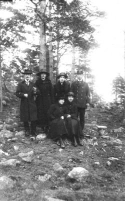 2 män och 2 kvinnor stående och 2 kvinnor sittande i skogsbacke.
Nyckelord: Skogsbacke