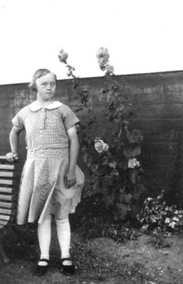 Flicka stående framför mur.
Nyckelord: Parkbänk Blommor Mur