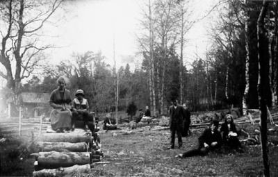 Personer sittande eller stående i hage.
Nyckelord: Ved