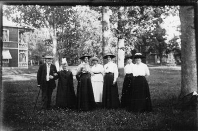 Man och 6 kvinnor stående i park.
Nyckelord: Gräsmatta Park Dräkt