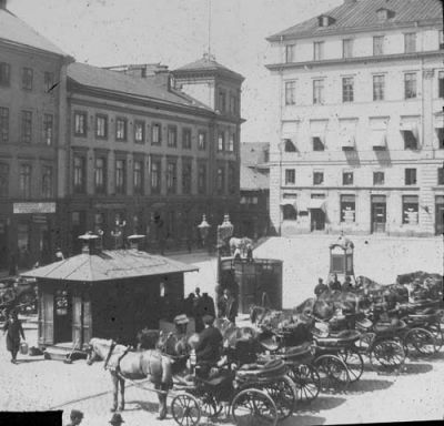 Hästekipage på torg
Nyckelord: Häst Vagn Telefonkiosk Toalett Gatlykta