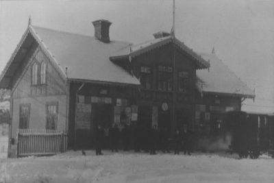 Ett grupp människor vid järnvägsvagn framför byggnad
Nyckelord: Järnvägsstation Tåg
