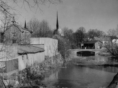Stadsvy med bro över vattendrag och kyrktorn i bakgrunden
