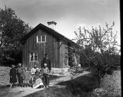 Man, kvinna och 5 barn samlade vid husgavel
Nyckelord: Familj vid hus