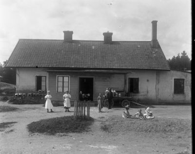 Män, kvinnor och barn på gårdsplan framför hus
Nyckelord: Mjölkkrukor Mjölkkärl Mejeri Hästkärra