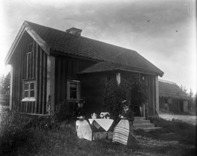 2 kvinnor sittande  i trädgård
Nyckelord: Kaffekopp Kaffekanna Duk