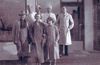 5 män och 2 kvinnor stående framför byggnad
