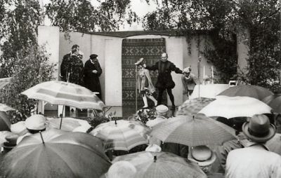 Ett antal människor under paraply ser på teater
Nyckelord: Paraply Teaterscen Skådespelare