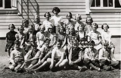 Kvinna och ett antal barn sittande och stående framför byggnad
Nyckelord: Skolfoto