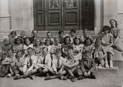 Kvinna och ett antal barn sittande och framför byggnad
Nyckelord: Elever Skolelever Skolbyggnad Skolklass Skolfoto Skolfotografi Klassfoto Klassfotografi