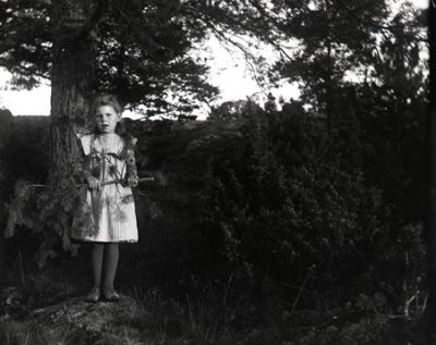 Flicka stående på sten invid tall
