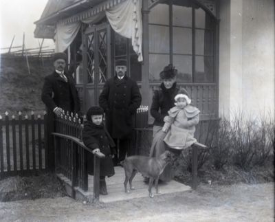 2 män 1 kvinna 2 flickor och 1 hund framför glasveranda
Nyckelord: Glasveranda Dräkt Hund Gärdesgård