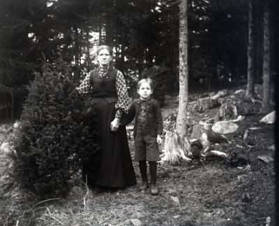 Kvinna som håller pojke i handen stående i skogen
Nyckelord: Dräkt
