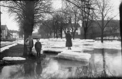 Kvinna stående på isflak i ån och 2 barn stående bredvid ån.
Nyckelord: Islossning