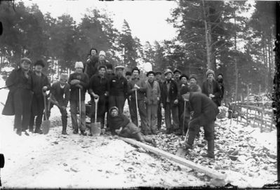 Ett antal män med spadar står uppställda i Ramunderskogen vid vägbygge.
Nyckelord: Vinter Spade