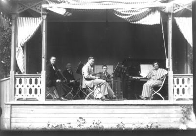 3 män, 1 pojke och 1 kvinna sittande på estrad.
Nyckelord: Musikkapell Instrument