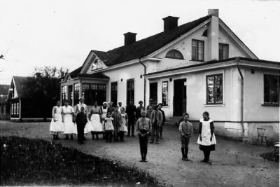 Byggnad med ett antal stående personer framför.
