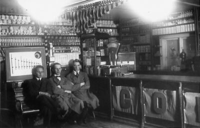 3 män sittande i affär.
