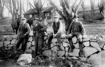 4 män stående och sittande vid stenmur.
Nyckelord: Stenmur