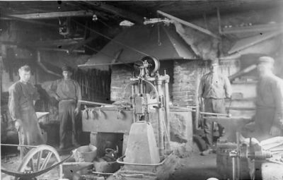 4 män stående i smedja.
Nyckelord: Smedja