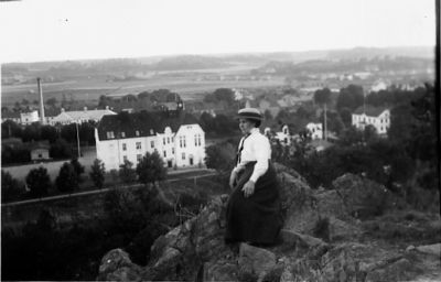 Kvinna sittande på berg med byggnader i bakgrunden.
Nyckelord: Utsikt Dräkt Hatt