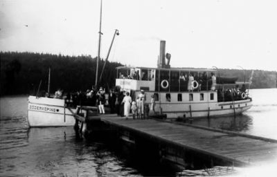 Ett antal personer gående av och på båt som ligger vid brygga.
Nyckelord: Skärgård