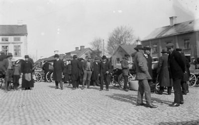 Ett antal personer på torg.
Nyckelord: Torghandel